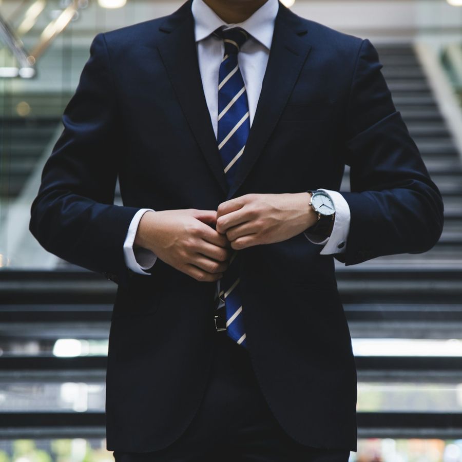 A man in a navy suit buttoning his jacket
