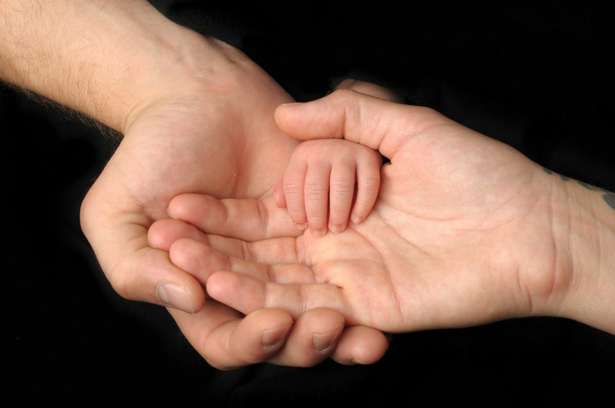 An adult's cupped hands holding a baby's hand